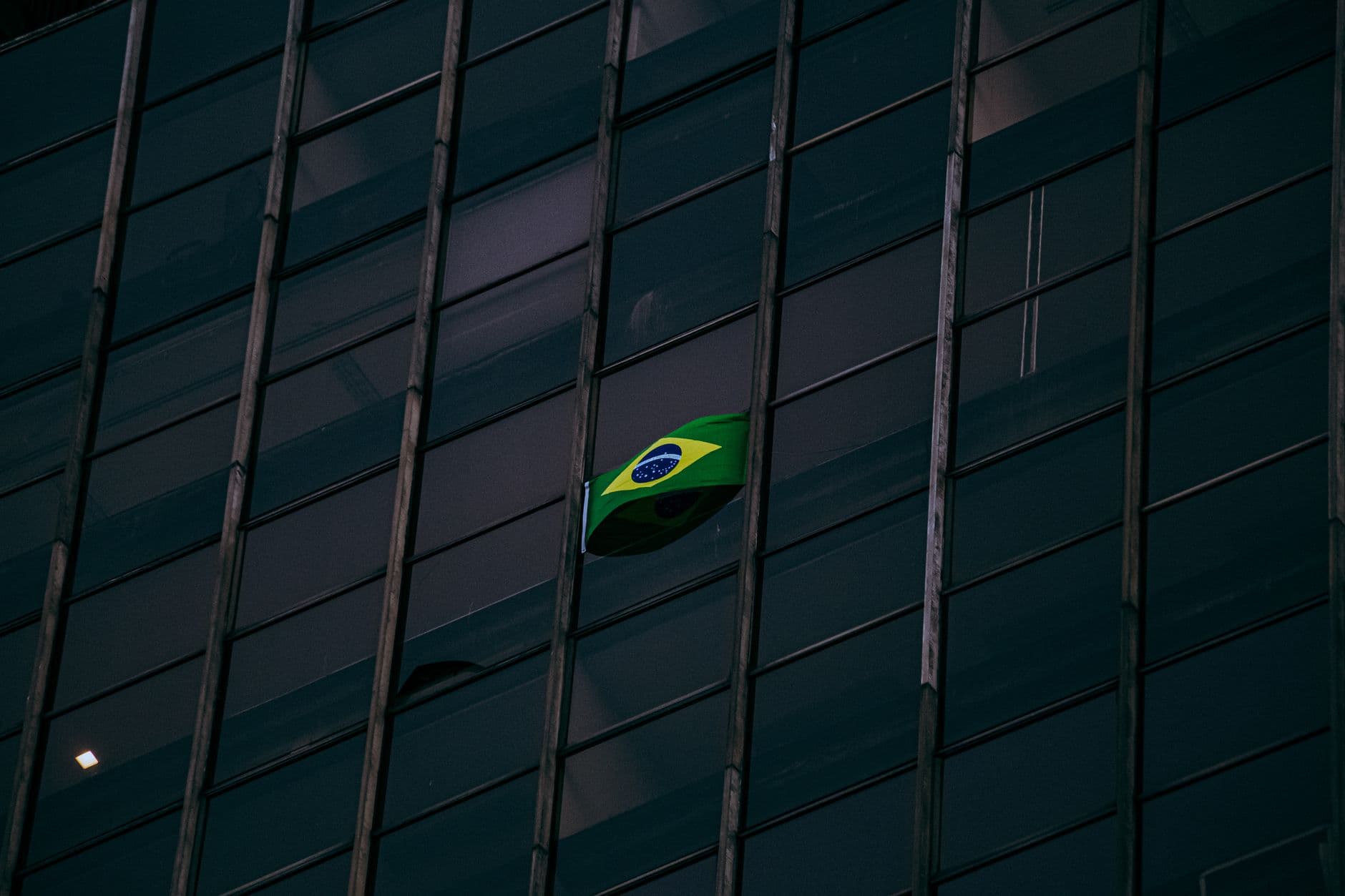 Brazilian flag displayed on a modern office building facade at night.