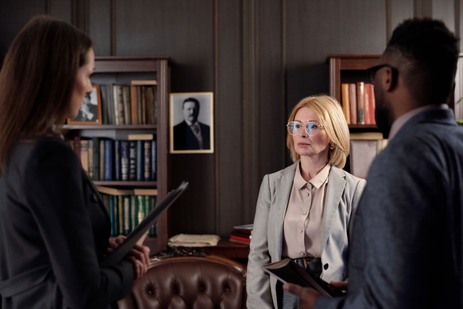 Three business professionals engage in a serious meeting in an executive office setting.